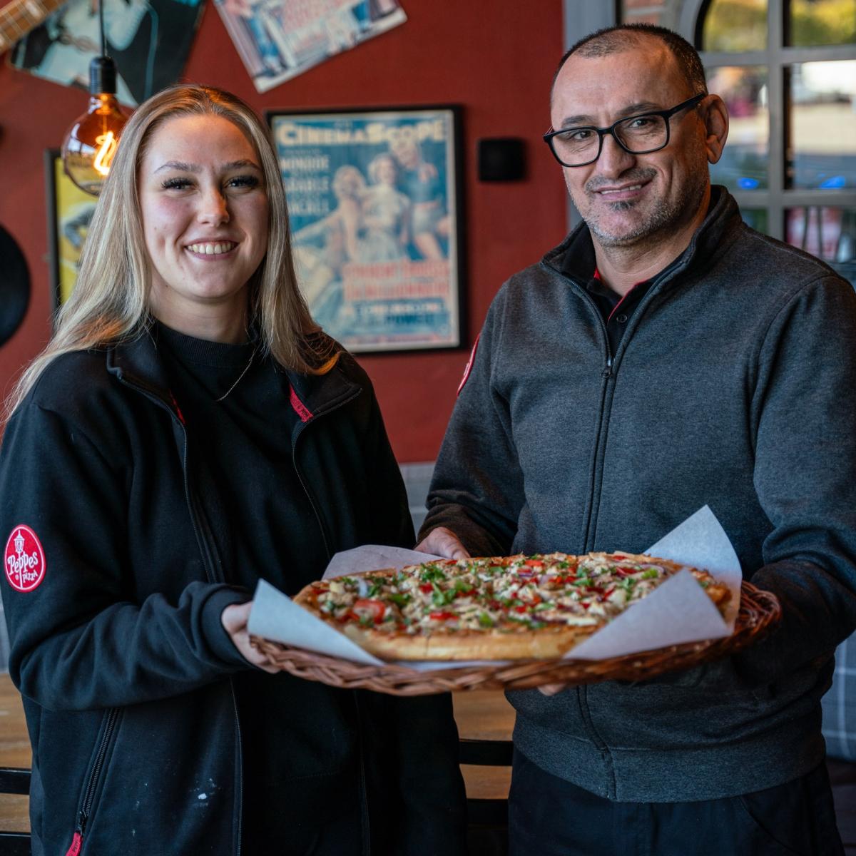 To ansatte med en pizza i hånden hos Peppes pizza i Sarpsborg. Foto.