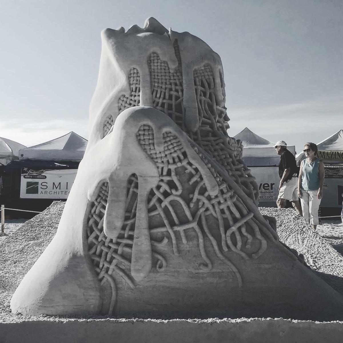 Black and white image of a sand sculpture that depicts an unclear sculpture that is melting. Under the melting is some webbing.