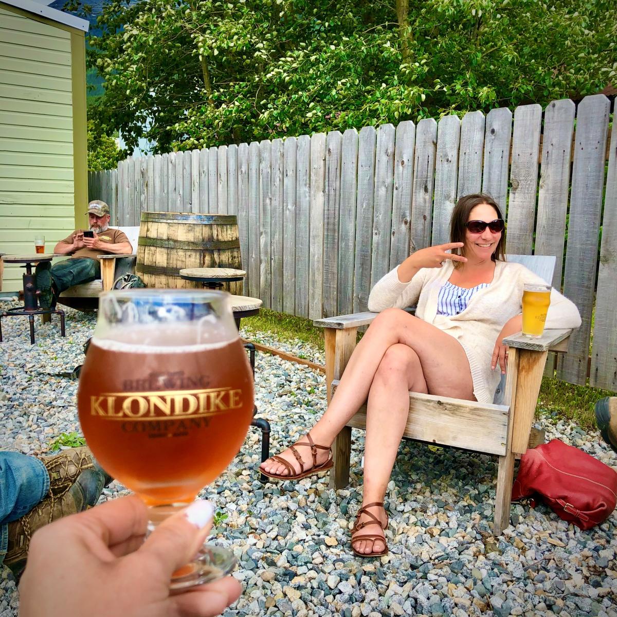 Glass raised to lady enjoying a beer and flashing the peace sign outdoors at Klondike brewing