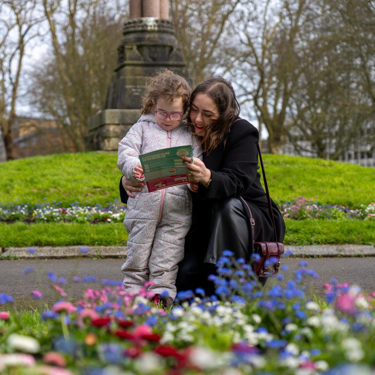 Mother kneeling down smiling next to young daughter whilst holding Easter Trail map in Southampton Park