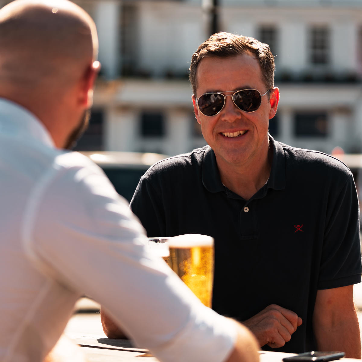 Smiling man sat outside at Dancing Man Brewery with a pint and some friends