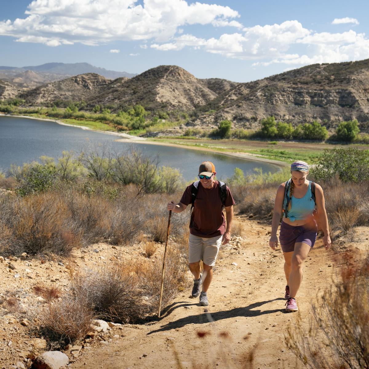 A man and a woman hike alongside a lake