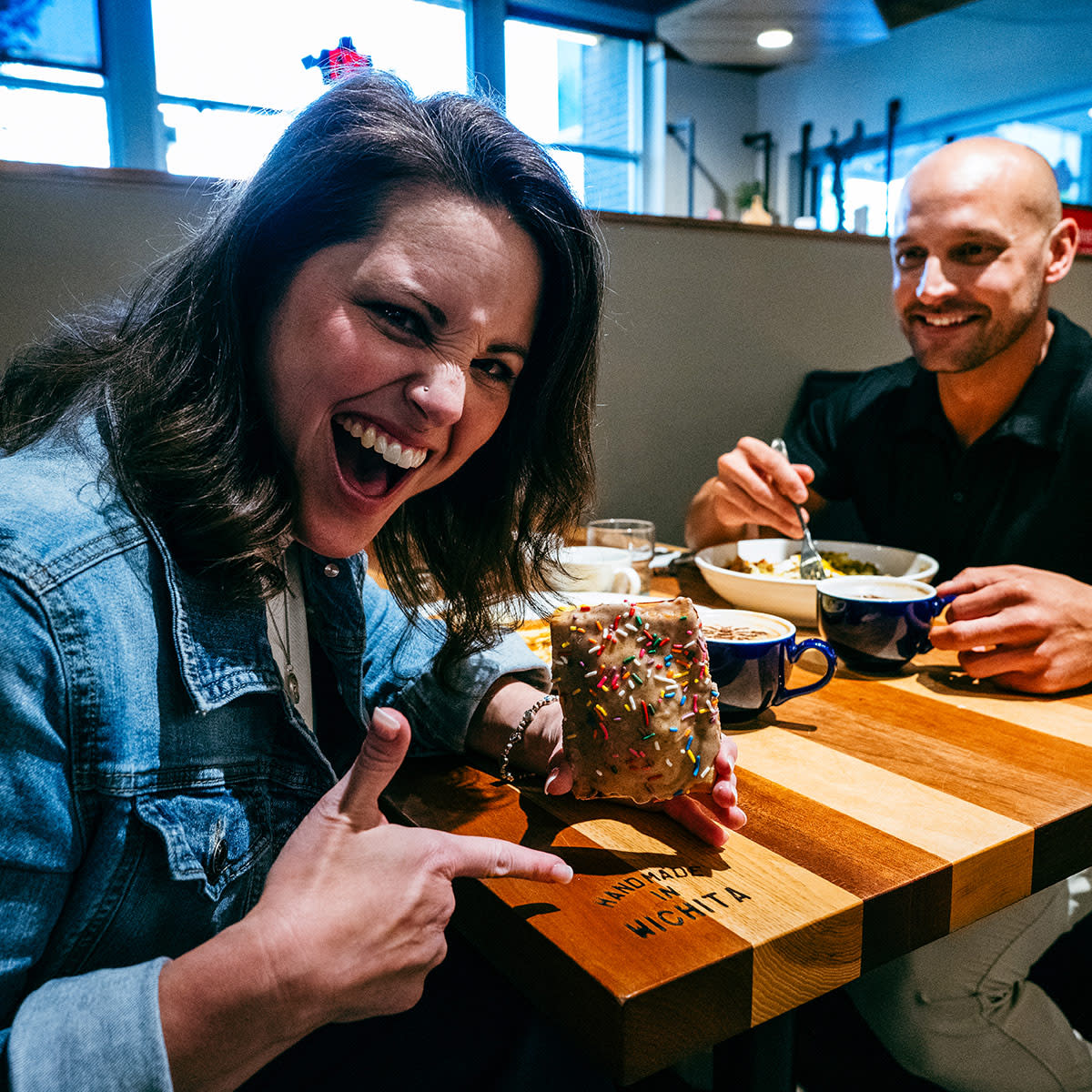 A woman smiles and points to her pastry while a man smiles at her at HomeGrown.