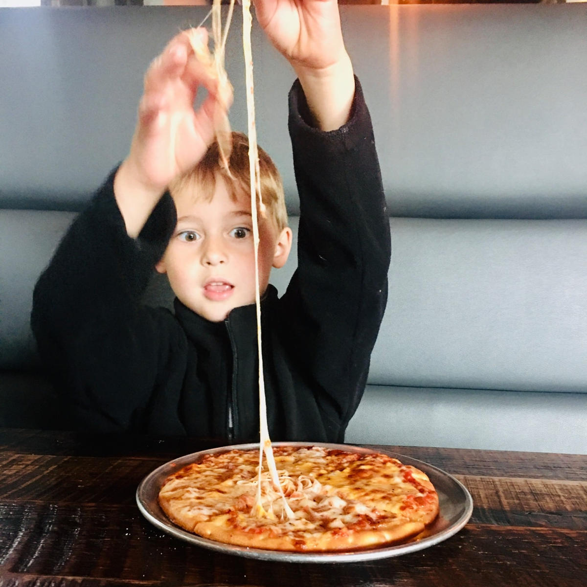 Boy pulling cheese pizza at Crust