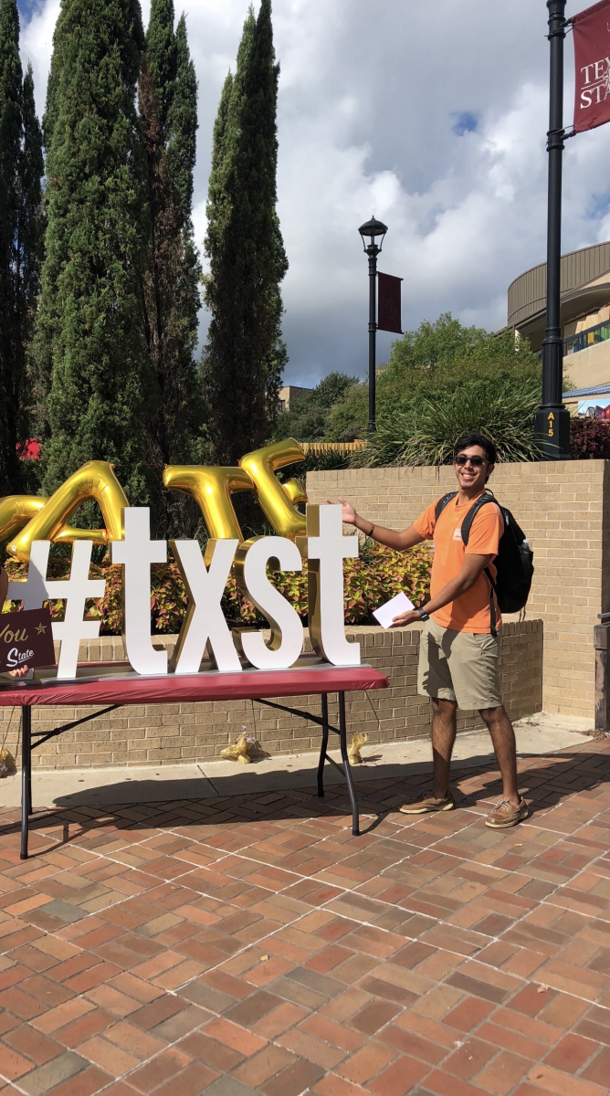 Luis Dominguez poses with the #txst sign on the Texas State University campus in San Marcos, Texas