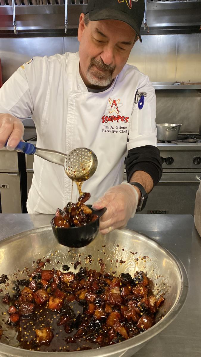 Albuquerque Isotopes Executive Chef Jim Griego scoops some pig candy from a large mixing bowl into a baseball helmet cup.