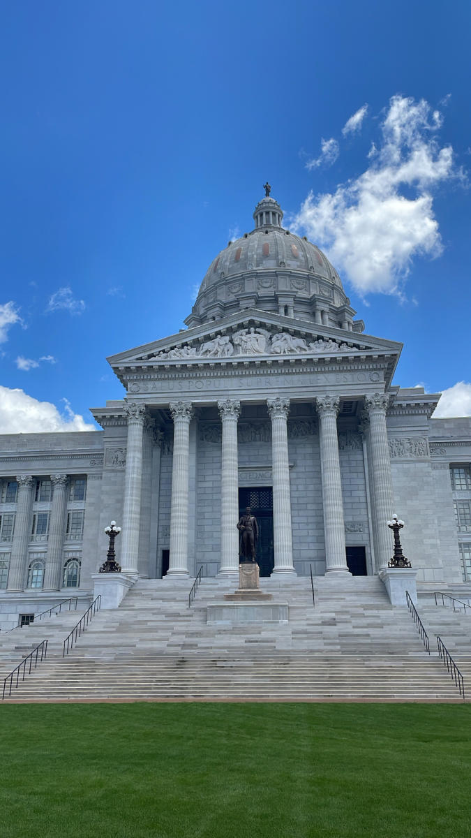 south lawn of the Missouri State Capitol with green grass, grand staircase and dome against blue sky