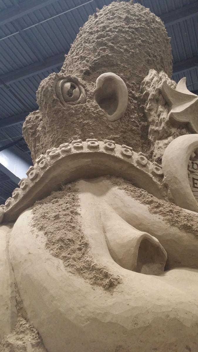 Up close image of a large sand sculpture depicting an octopus face and tentacles