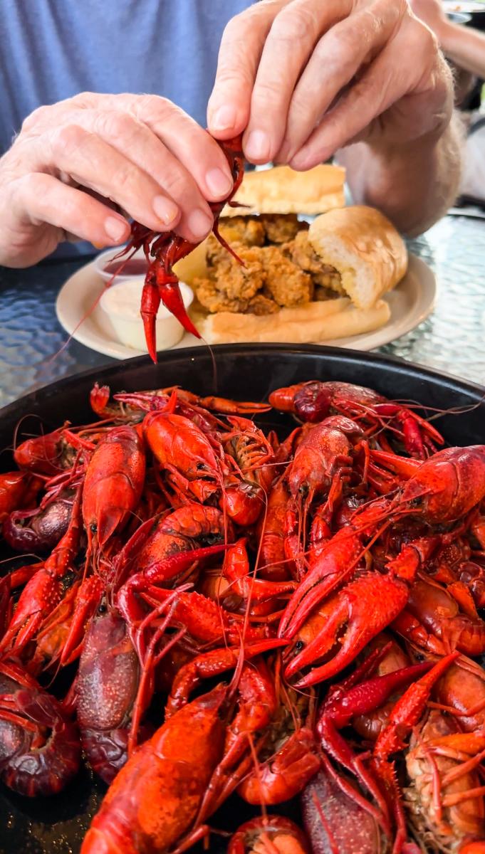 A pair of hands pulls apart a boiled crawfish above a loaded tray of crawfish, corn, potatoes and lemons at Morton's Seafood Restaurant