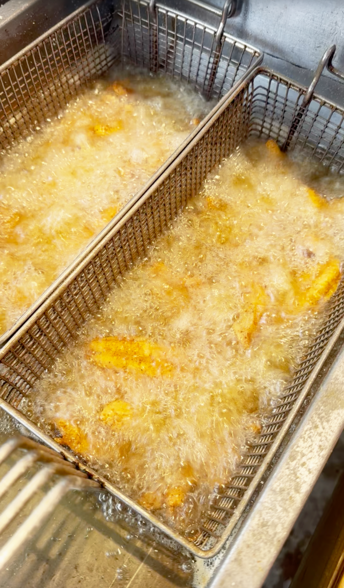 Two large metal baskets containing seafood or fresh fish, boiling in hot oil.