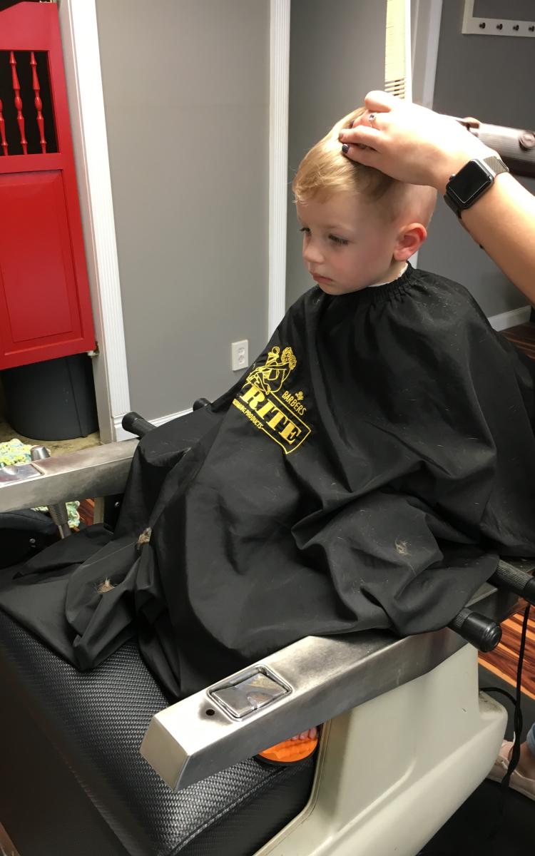 A young boy sits in a booster chair for a haircut
