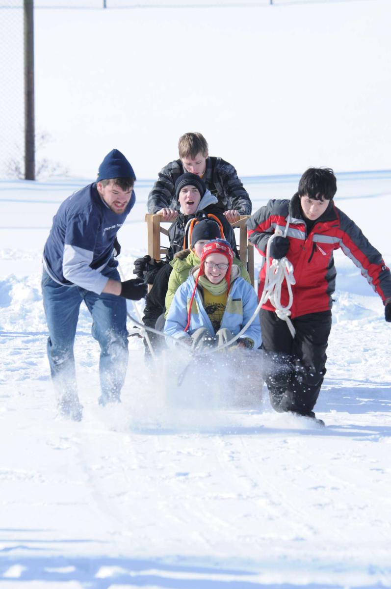 A team of students pull a dog-sled in the snow.