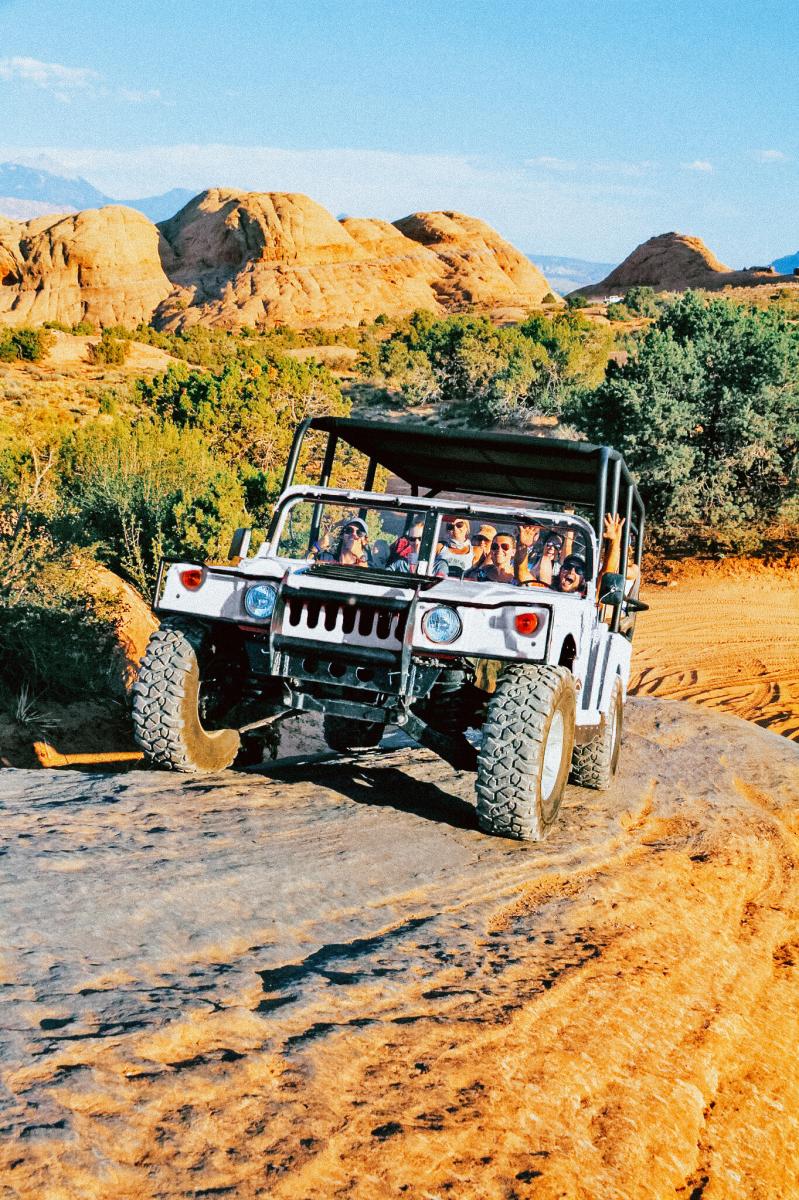 A white hummer crawls over Moab’s red rock desert.