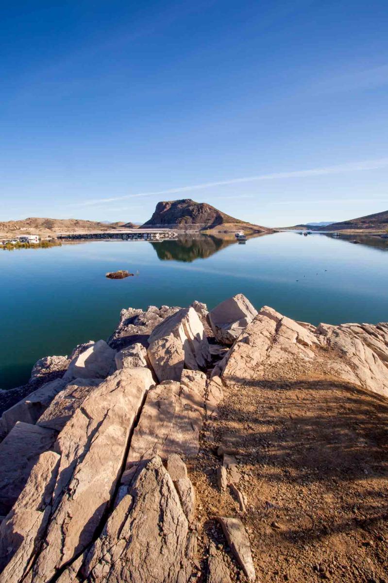 View of Elephant Butte Lake with clear blue skies and rugged foreground rocks.