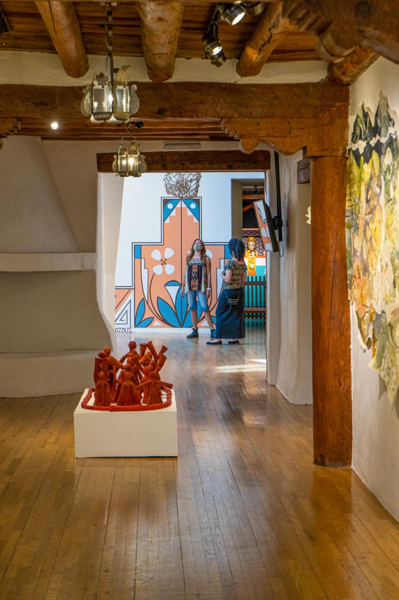 Interior view of an art museum, displaying vibrant artwork including a large mural and sculptures. A person stands in the doorway in the middle of the room, observing the pieces.