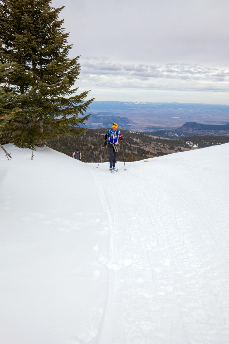 A person cross-country skiing on a snow-covered mountain slope with a scenic panoramic view in the background.