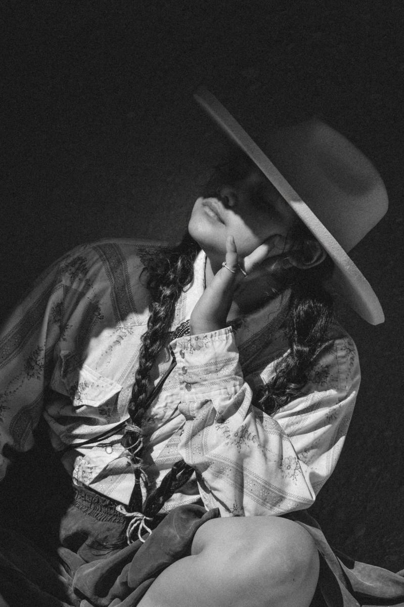 Black and white portrait of a seated figure wearing a wide-brim hat.