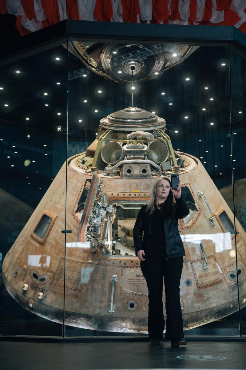 A woman taking a photograph in front of "Casper: The Apollo 16 Command Module" at the US Space and Rocket Center