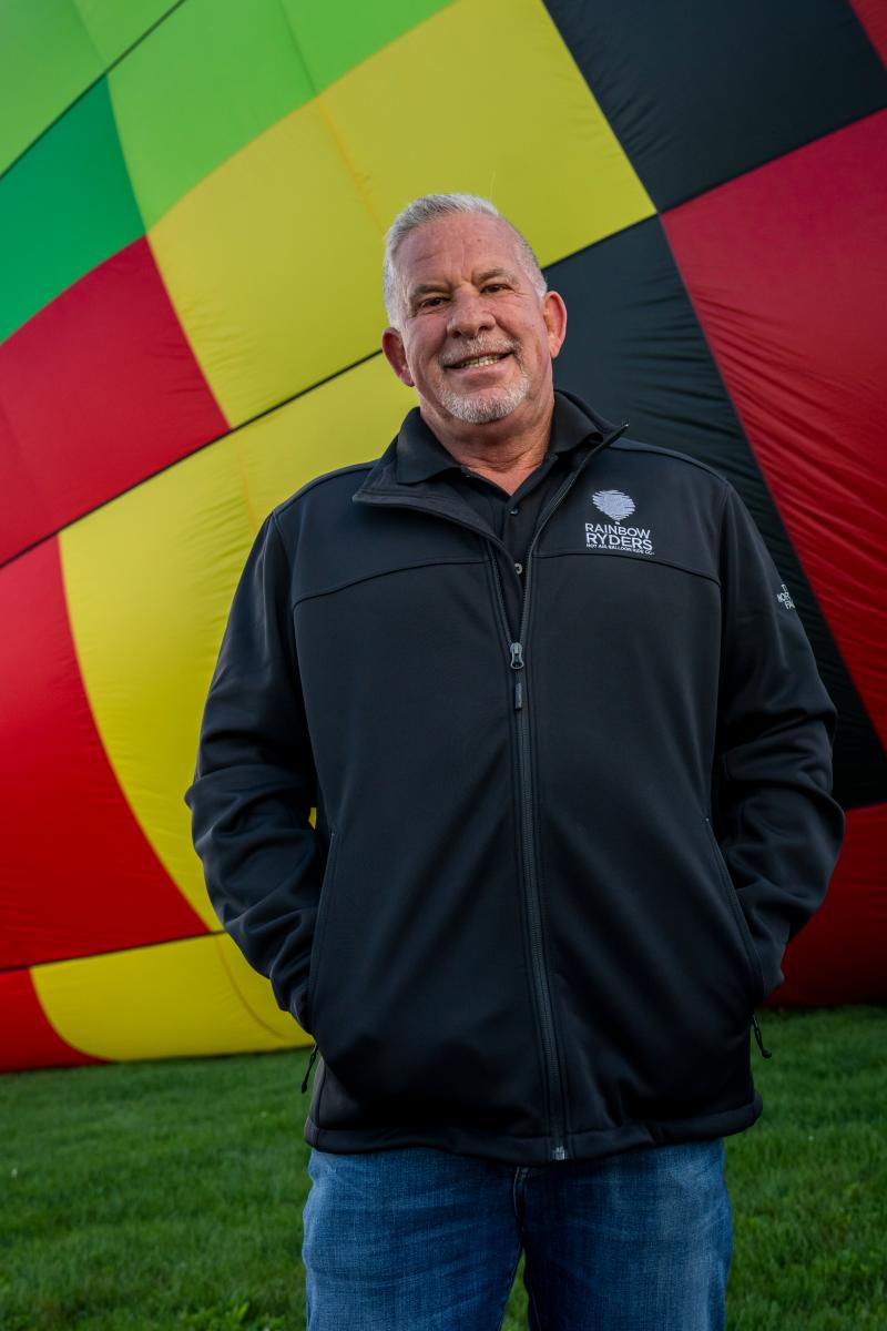 A photo of Rainbow Ryders Scott Appelman in front of the Visit Albuquerque hot air balloon.