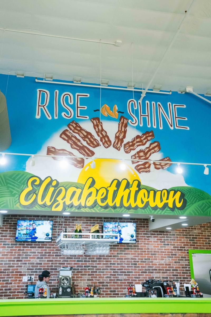 A mural of an egg symbolizing the sun with rays of bacon strips with the words "rise and shine" above the egg and bacon "sun" and Elizabethtown written below