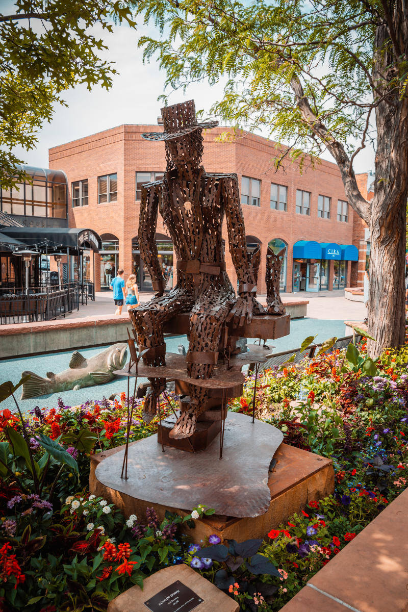A metal art sculpture of a man sitting on a chair in a garden.