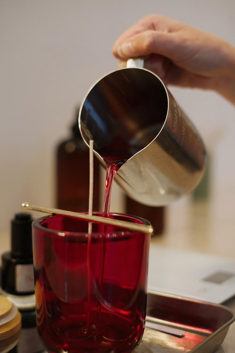 Someone pouring wax into a red, glass candle jar.