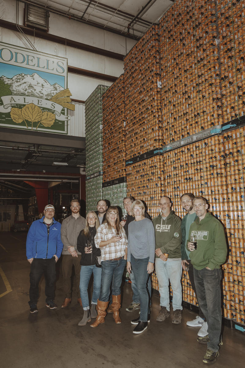 A group of people standing in front of a wall of Odell beer cans.
