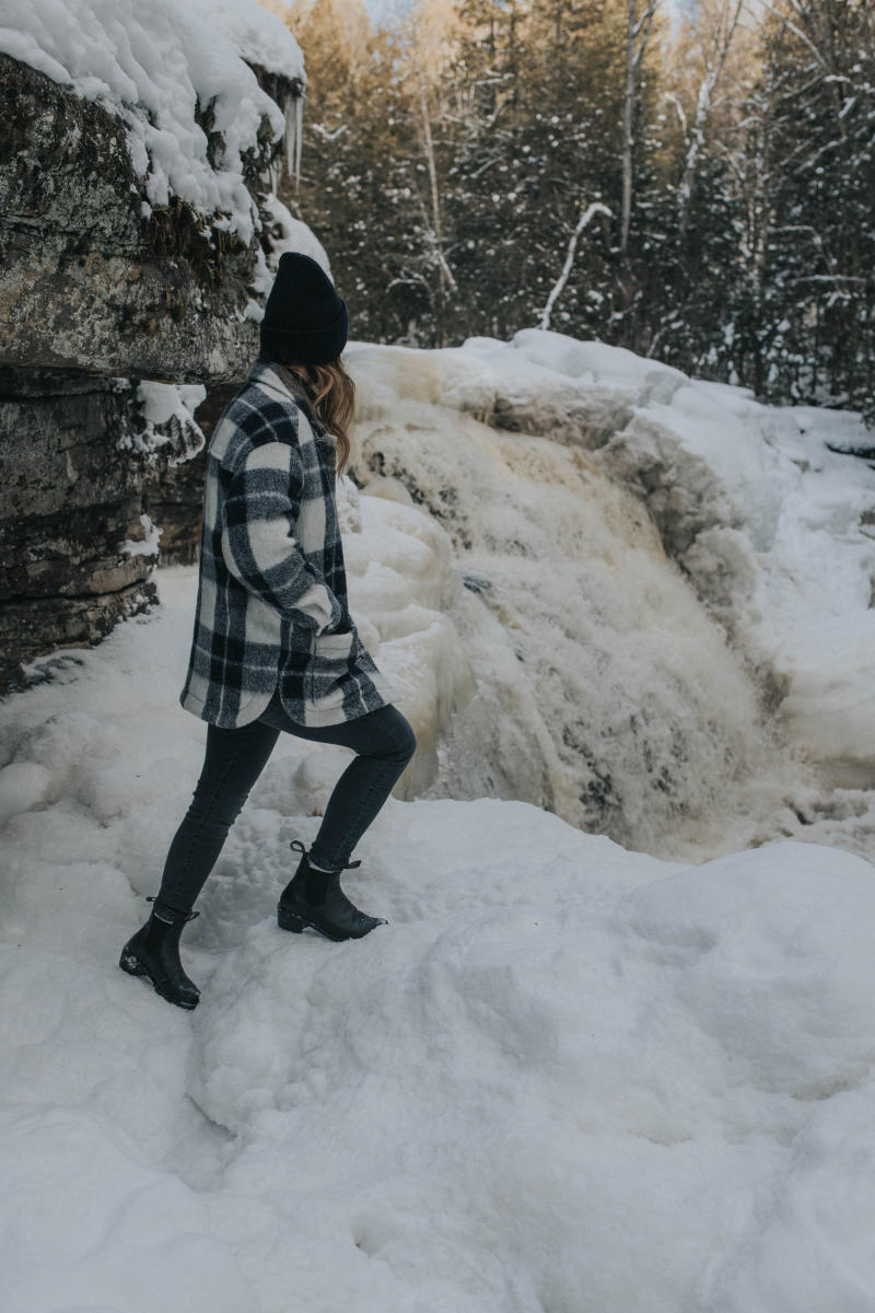a person stands in snow next to a waterfall flowing through ice and snow