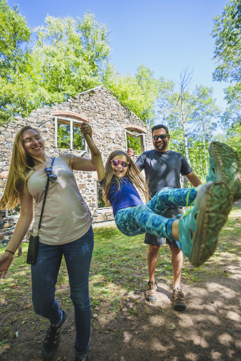 A mother and father joyfully swing their daughter in front of ruins.