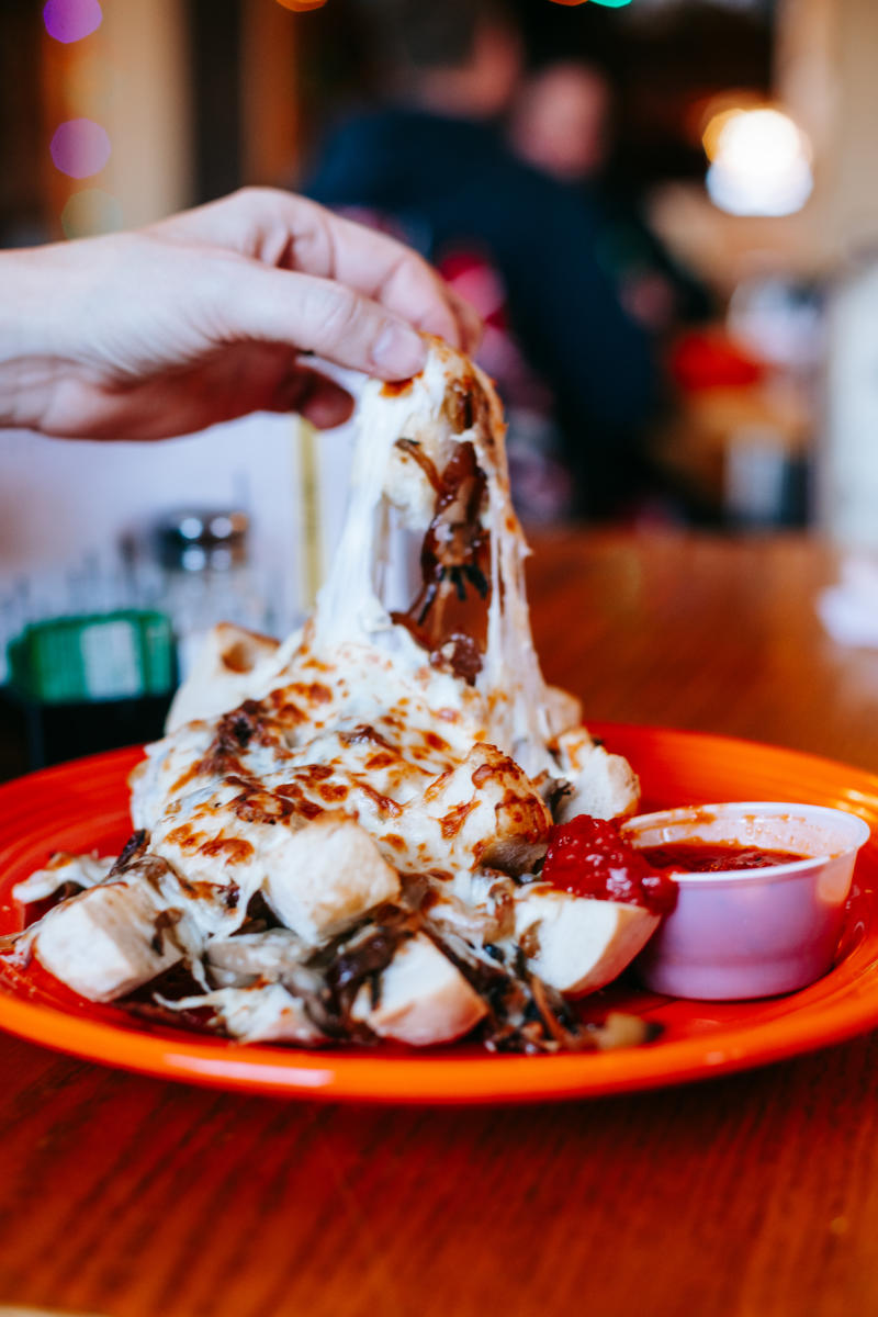 a hand pulls a cheesy bite from a plate