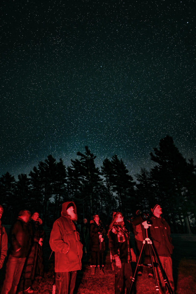 a group of people illuminated in night friendly LED lighting look up into the starry night sky