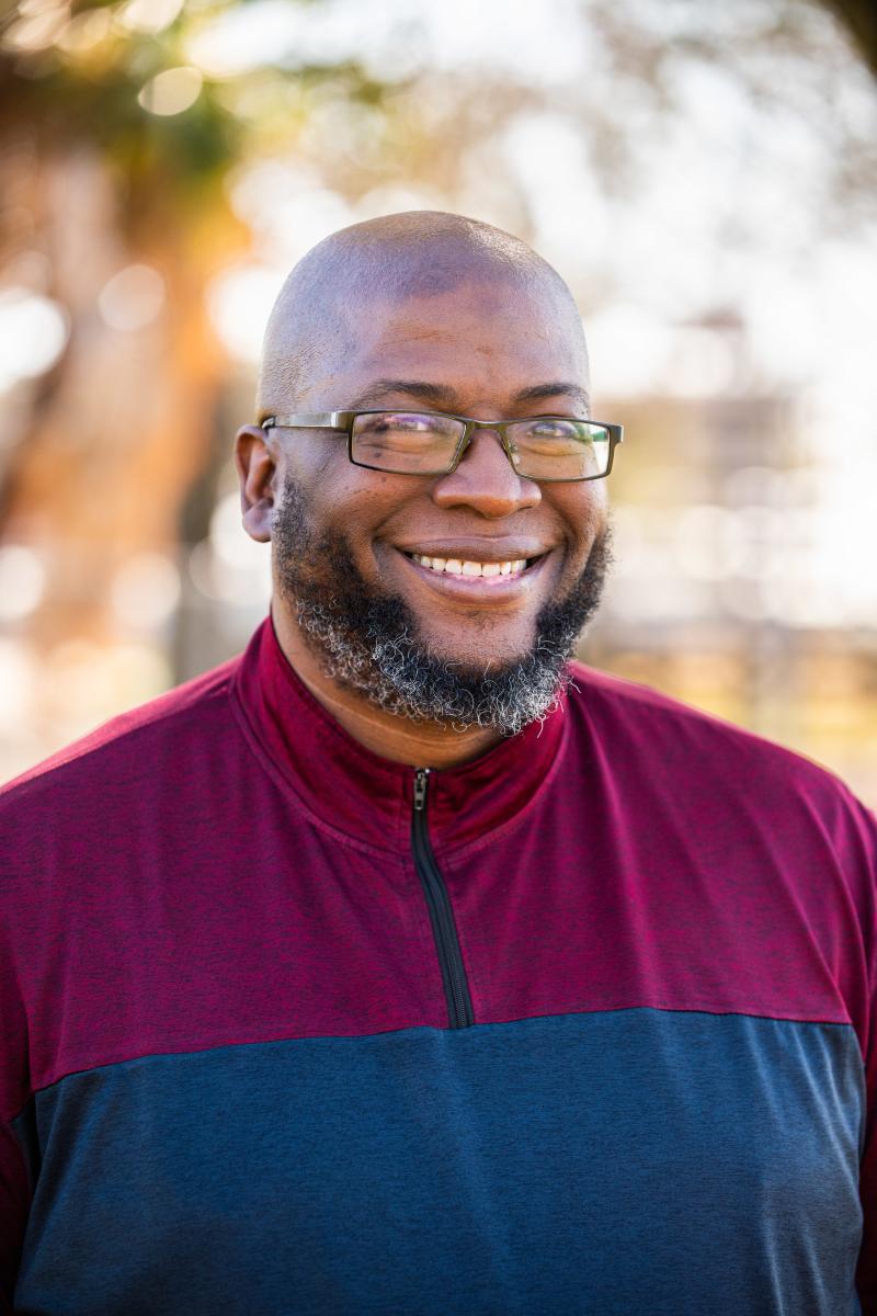 black man in glasses wearing a red and blue shirt in a professional headshot photo