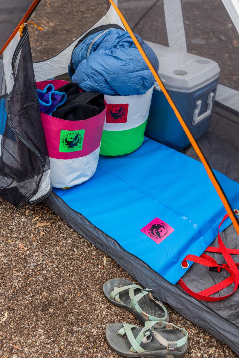 Camping gear inside a tent, a blue sleeping bag, a cooler, a blue mat, and a pair of sandals