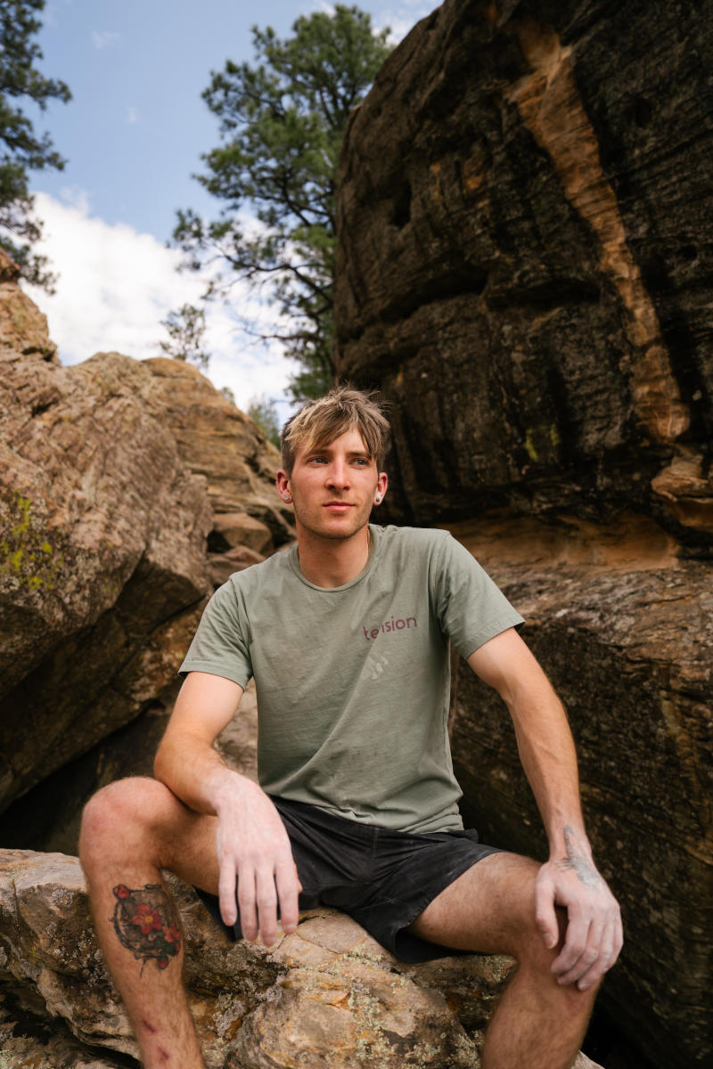 Climber, Ben Hanna, sits between cragged rocks while looking at the camera