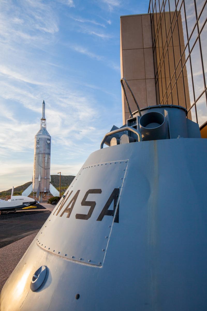 NASA rocket on display at a space center, with a close-up view of the side of a spacecraft featuring the NASA logo, set against a clear sky.