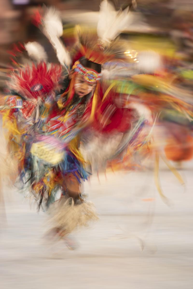 A dancer in colorful regalia captured in motion blur during a performance.