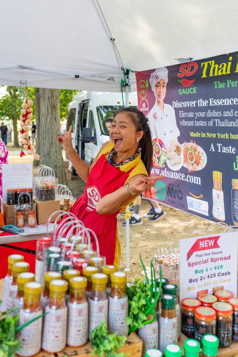 Woman smiling holding a peace sign up to the camera while selling her bottles of hot sauce at the chile pepper festival