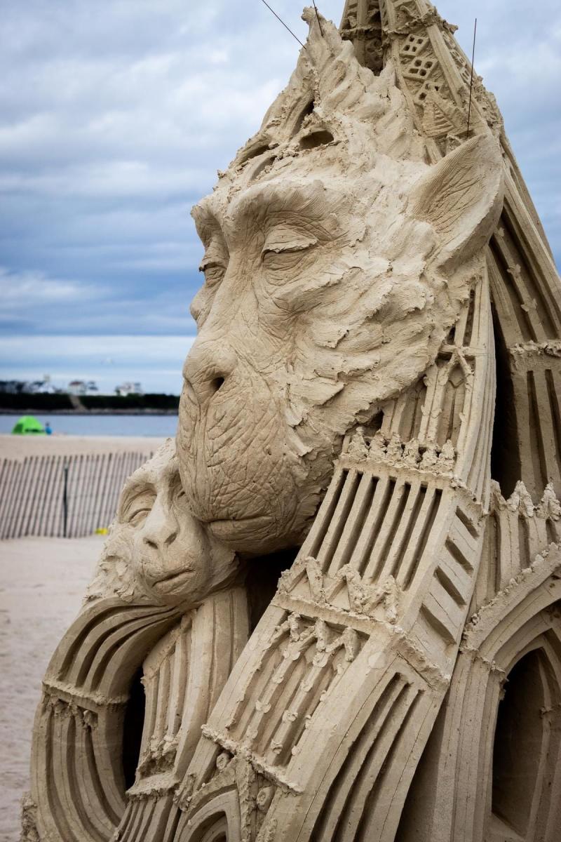 Sand sculpture of a mother monkey holding on to a baby monkey. Their bodies seem to be sculpted to look like buildings.
