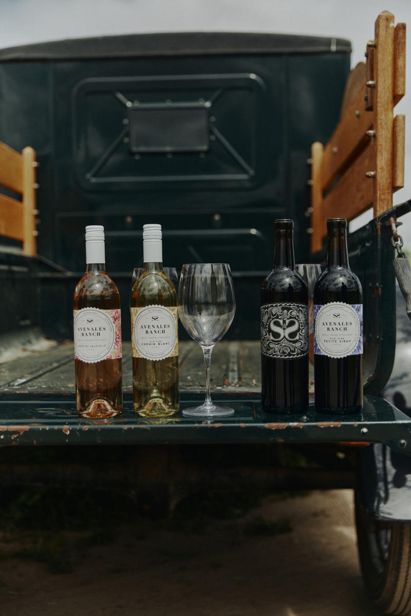 Four bottles of wine and a wine glass sitting on a tailgate of a classic truck.