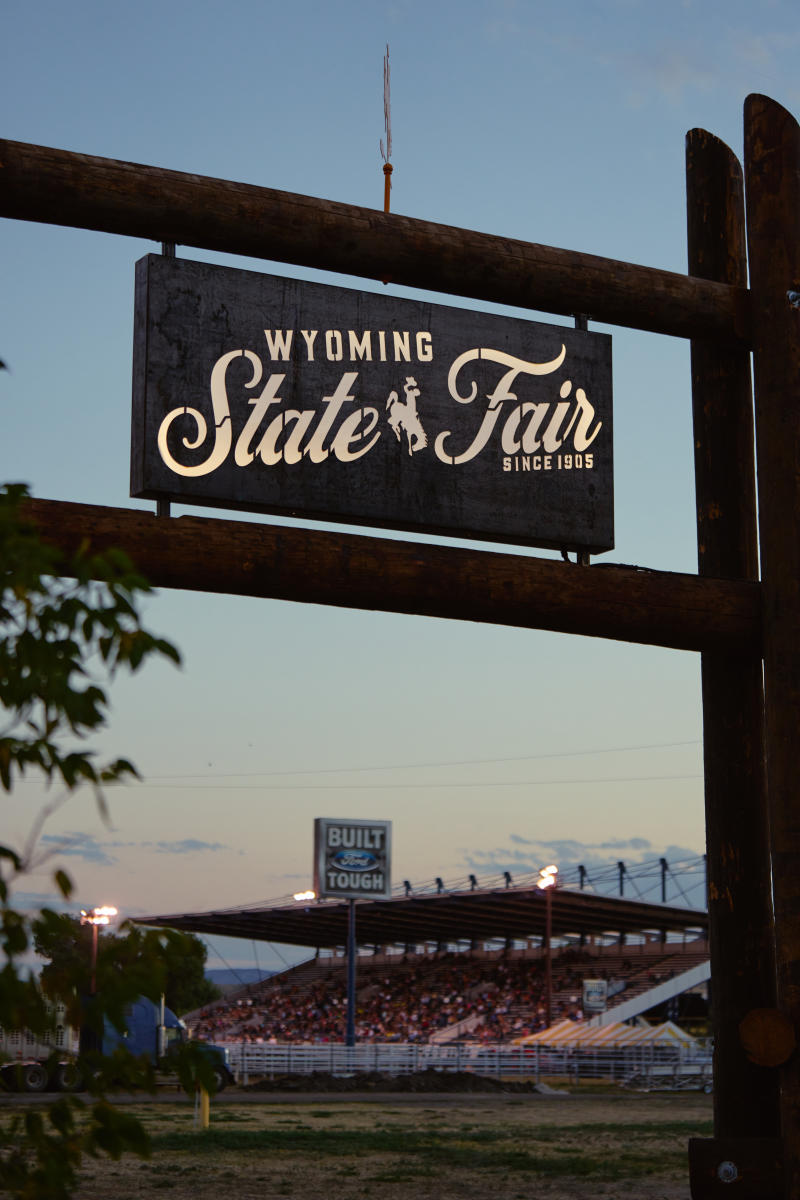 A sign, "Wyoming State Fair" with a backdrop of the fairgrounds at sunset in the background.