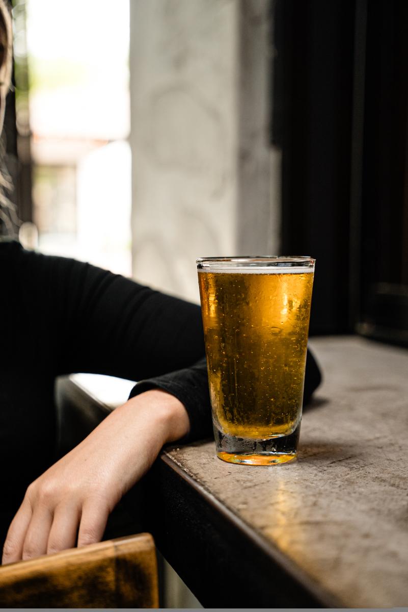 A young woman casually rests her elbow on the bar next to a glass of beer at Bosscat Kitchen & Libations.