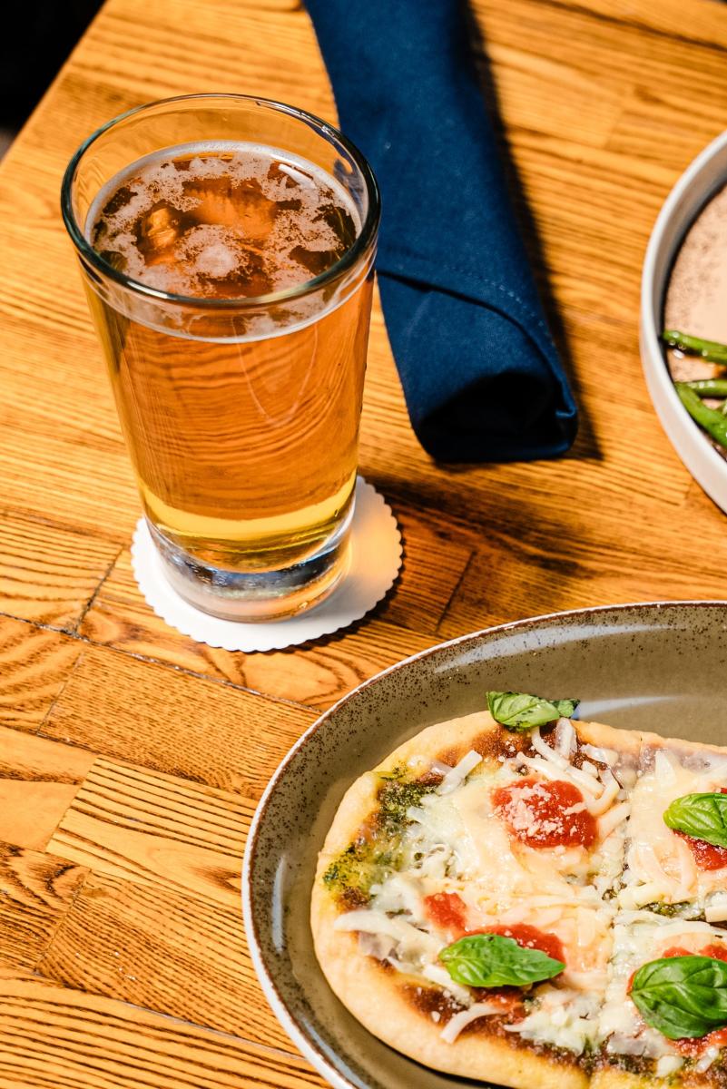 A glass of beer rests beside a pizza on a table at Bosscat Kitchen & Libations.