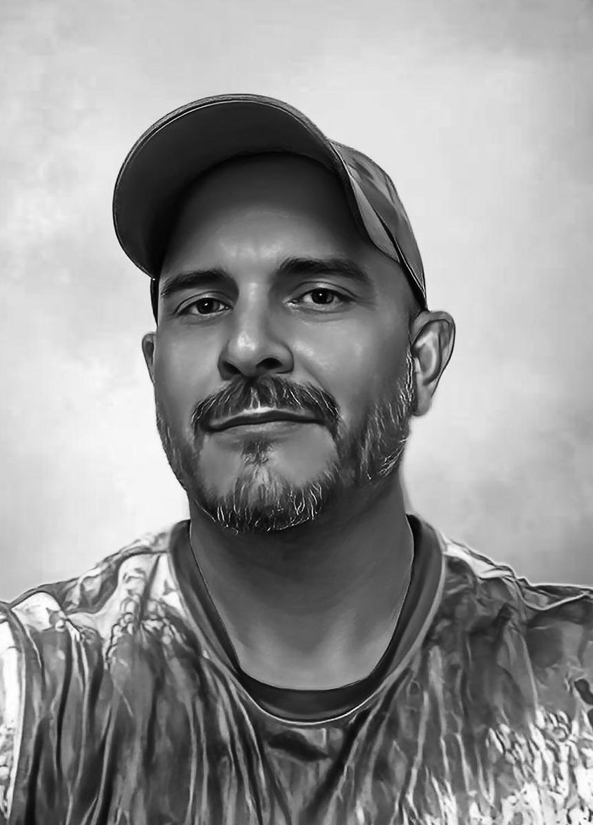 Black and white headshot of a bearded man in a baseball cap soft smiling at the camera.