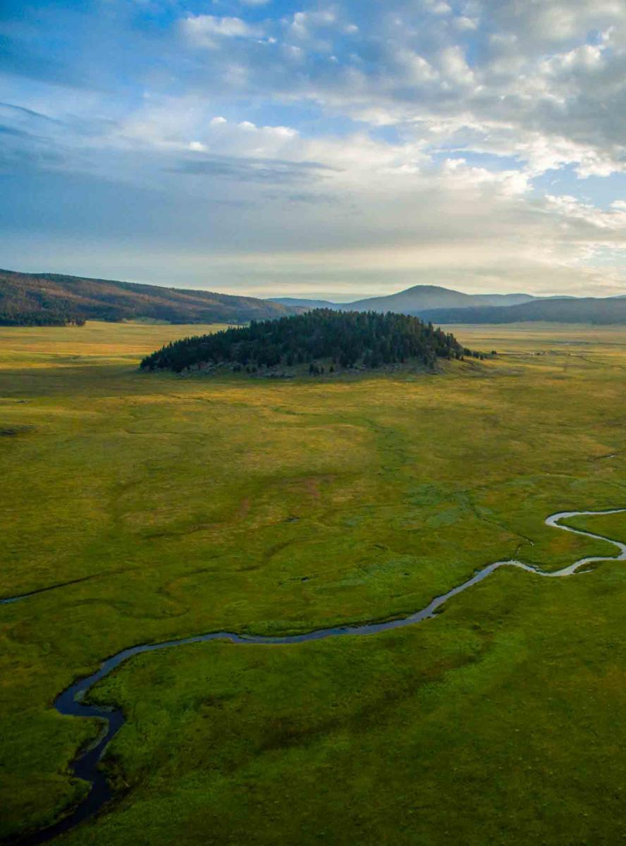 Aerial view of a meandering river flowing through a vast valley with patches of forest under a cloudy sky.