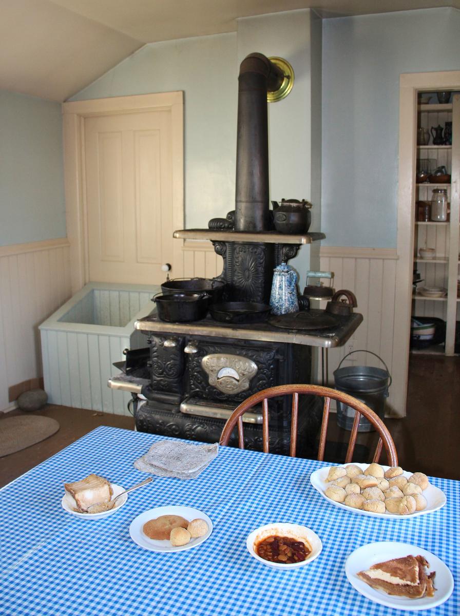 An old fashioned black stove sits behind a table with a blue tablecloth