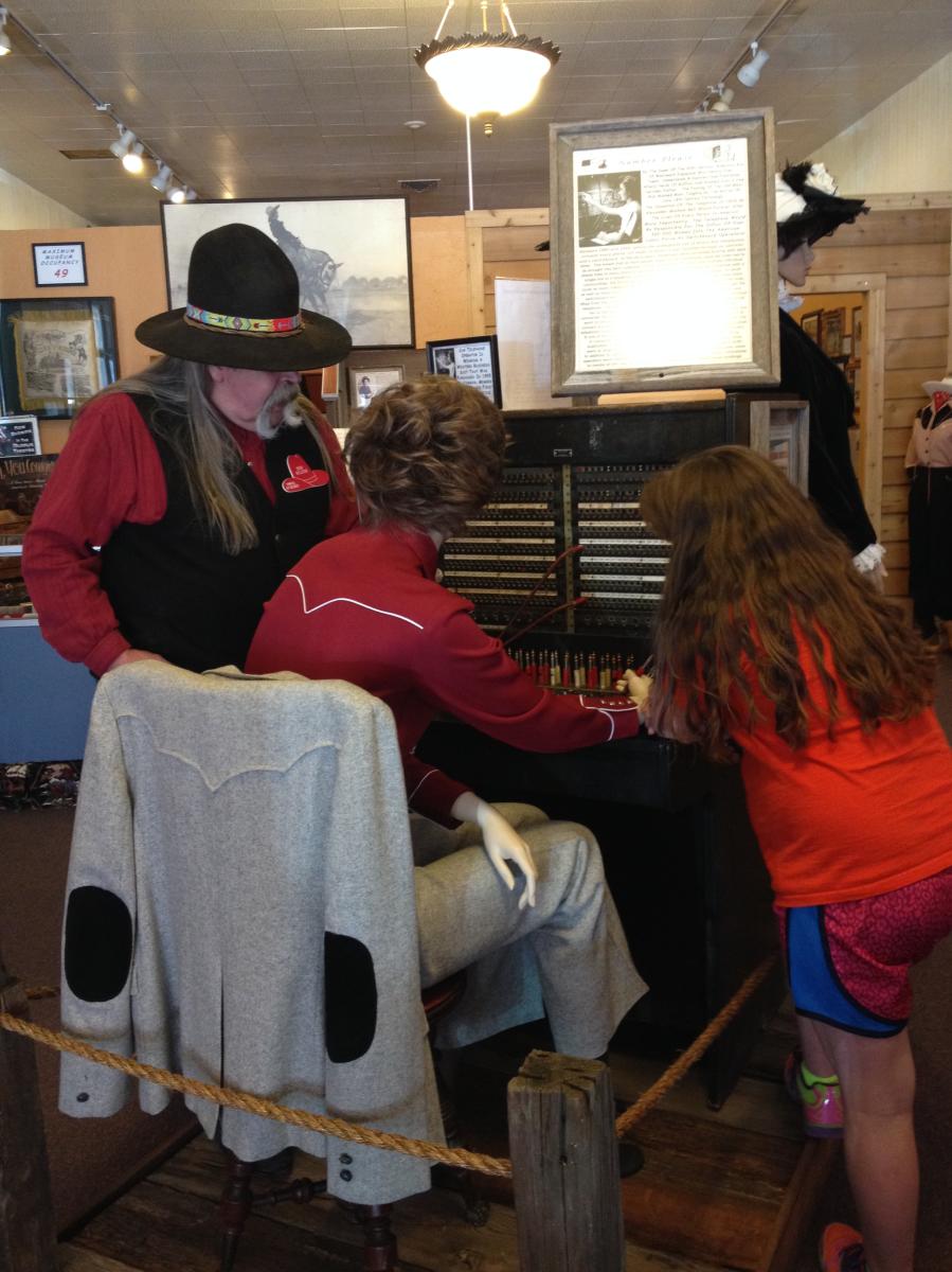 Western-dressed tour guide explains to young girl how operating boards worked with a museum display featuring a mannequin.