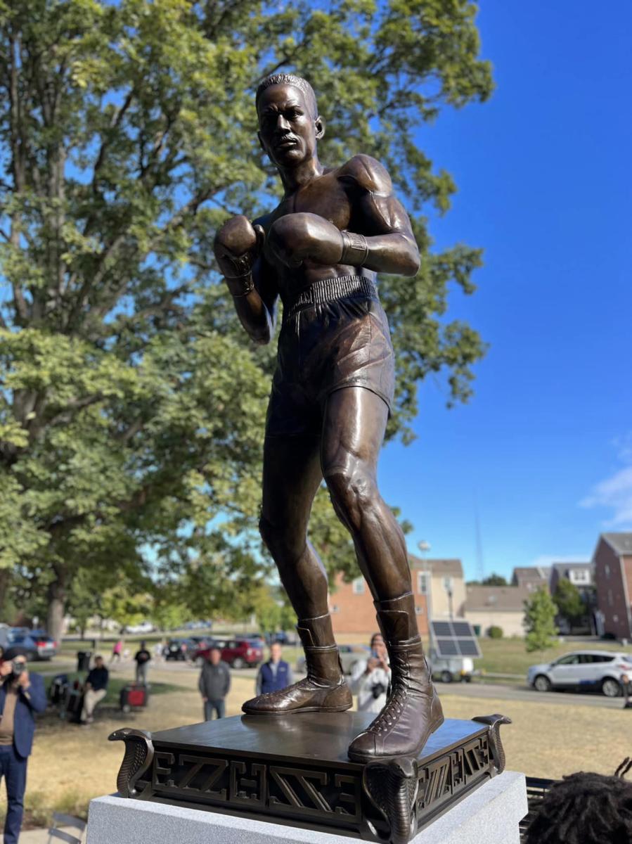 A metal statue of boxer Ezzard Charles with blue sky and a green tree in the background