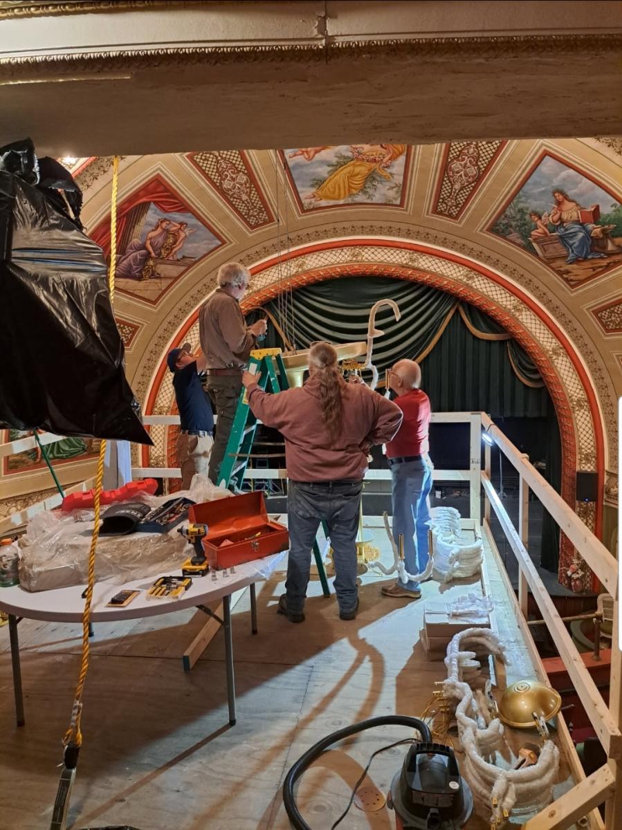 four people circle around a work in progress under the dome of a historic theater stage