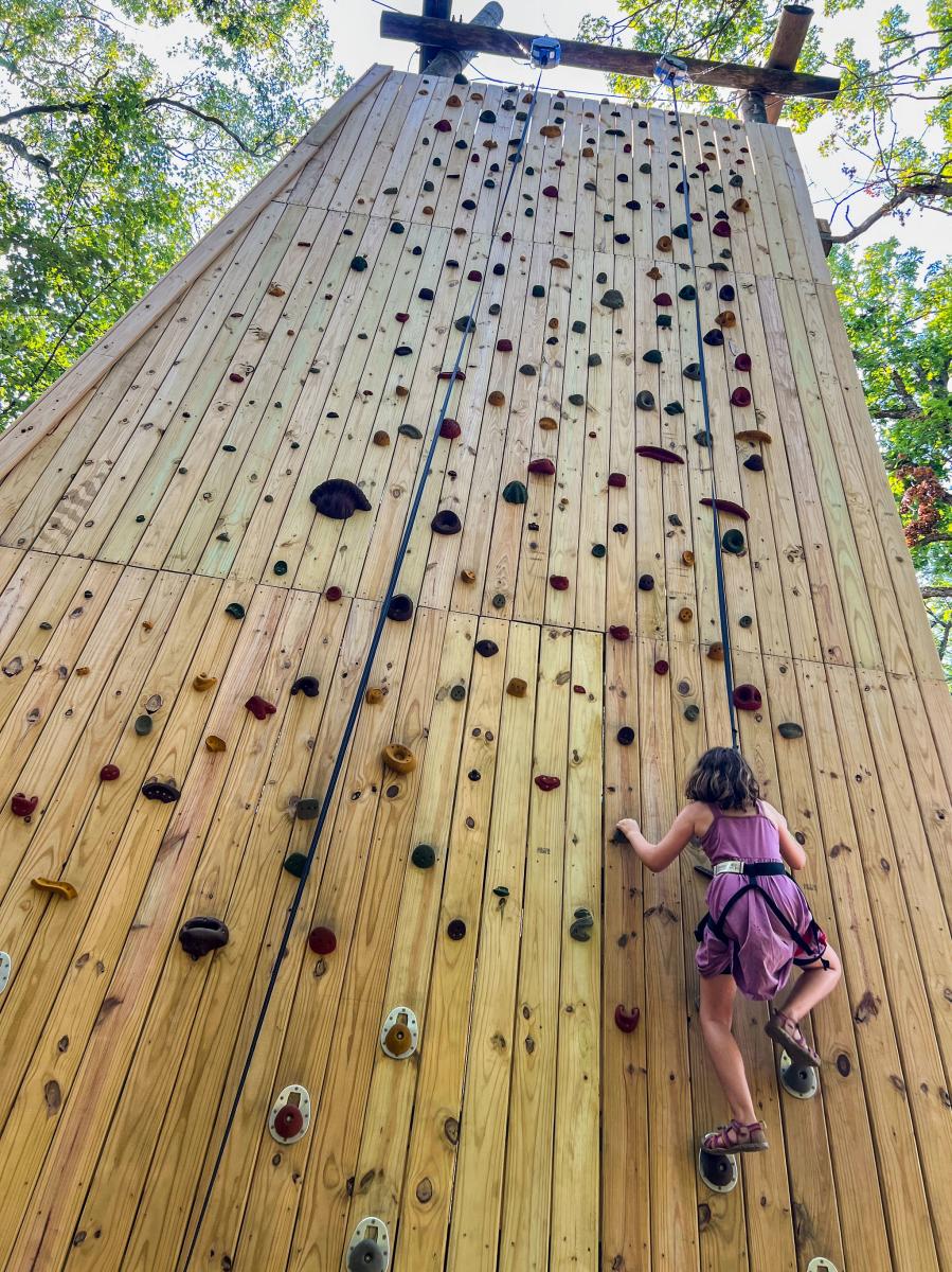 A young climber ascends a wooden climbing wall at the Muskegon Luge Adventure Sports Park.