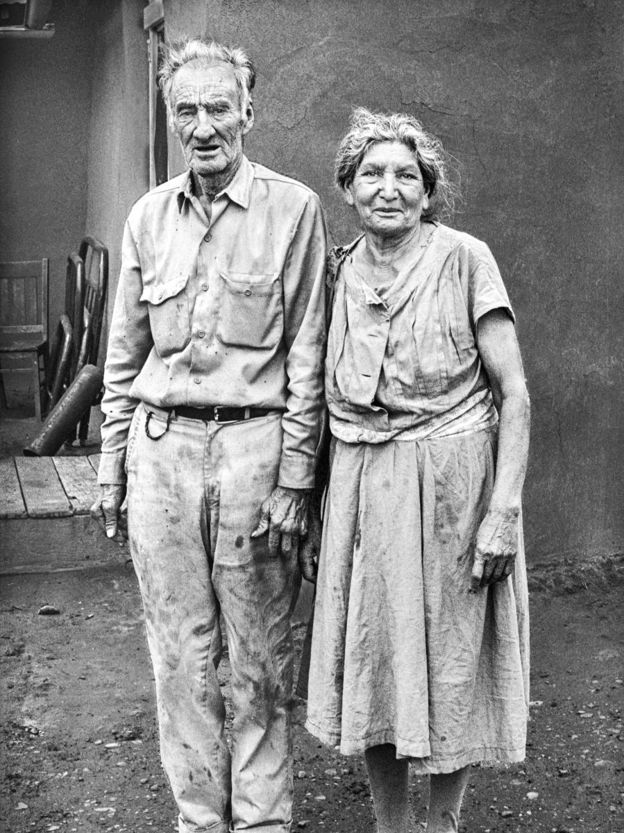 Black and white portrait of an older couple standing side by side outdoors, facing the camera.